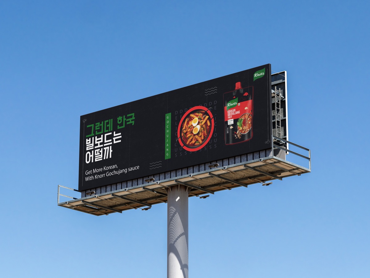 A black billboard at dusk carrying the Korean headline “그런데 한국 빌보드는 어떨까” beside a bowl of tteokbokki.