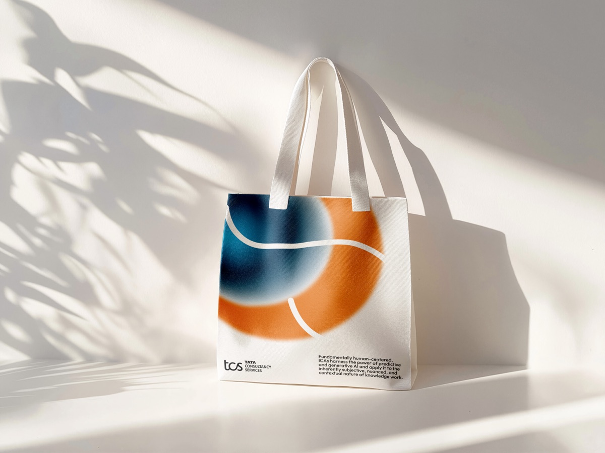 A canvas tote bag carrying the blue and orange gradient mark, under leaf shadows.